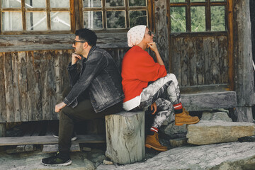 Couple sitting back to back in front of the house. Two sulky adults turned away from each other.