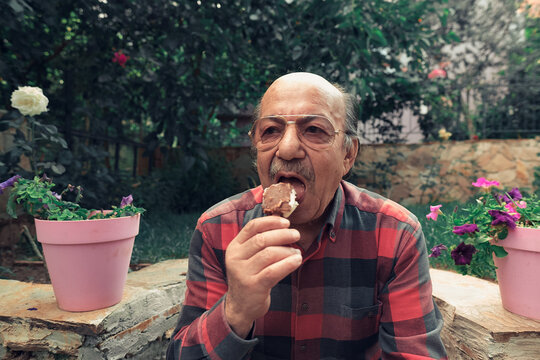 Close-up Portrait of senior man eating ice cream. Elderly man eating ice cream on stick in the backyard.