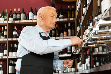Focused seller pouring wine from wine column in liquor store