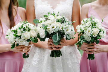 The bride and bridesmaids in an elegant pastel pink dress is standing and holding hand bouquets of ...