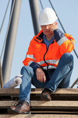Sad or depressed engineer or foreman with protective workwear sitting in front of an industrial...