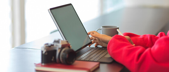 Female hands typing on tablet keyboard with camera and notebook on table