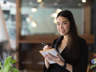 Businesswoman taking note on schedule book while standing in office room