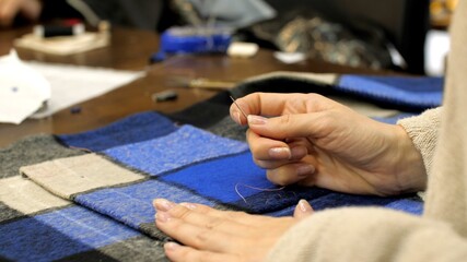 Sewing Studio. Tailor's hands are sewing on a piece of fabric with a thread and a needle. Close up. Female tailor in her workshop studio. Sewing up a hole in clothes. Clothing repair workshop