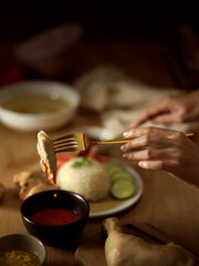 Woman eating Hainanese chicken rice, dipping chicken in the chilli sauce