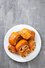 small buns with cinnamon on white plate on ceramic background