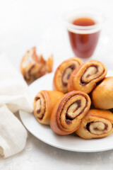 small buns with cinnamon on white plate and cup of coffee on ceramic background