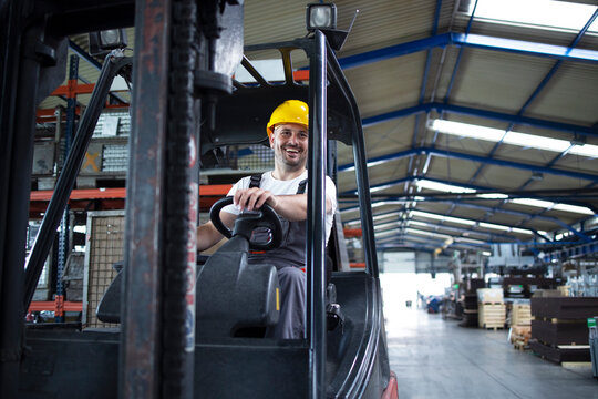Professional male industrial driver operating forklift machine in factory's warehouse.