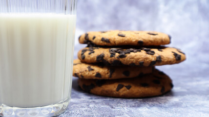 American chocolate chip cookies stacked on top of each other with milk in a glass on a gray background. Traditional rounded crunchy dough with chocolate chips. Bakery. Delicious dessert, pastries.