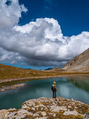 Fototapeta na wymiar Male tourist near the shore of a high mountain lake. Large white clouds and mountains are reflected in the turquoise water. Kazakhstan, Kensu gorge