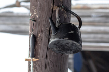 Vintage metal kettle hanging on wooden pillar. Old metal kettle, household utensils