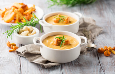 Mushroom cream soup with chanterelles and herbs on dark rustic wooden background.