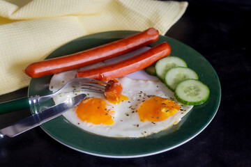 Breakfast with scrambled eggs, sausages and cucumber. On a dark background with a yellow napkin