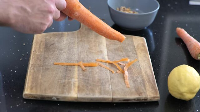 Close-up of peeling a large carrot over a wooden cutting board.
