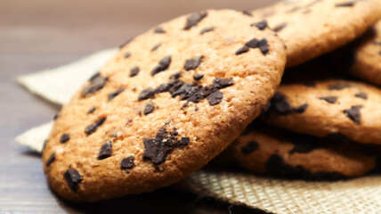 American chocolate chip cookies on a brown wooden table and on a linen napkin close-up. Traditional rounded crunchy dough with chocolate chips. Bakery. Delicious dessert, pastries. Rural still life.