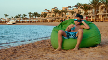 Teenage boy enjoying lemonade at coastline. Cute young man sitting at seaside.