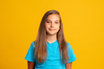 Obraz premium Happy childhood. Positive attitude. Kid lifestyle. Portrait of confident young girl in blue t-shirt looking at camera smiling isolated on orange copy space background.