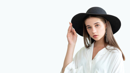 Trend summer outfit. Casual boho style. Beautiful woman in wide-brimmed black hat vintage earrings white blouse. Looking at camera isolated on neutral copy space. Female elegance. Fashion model look