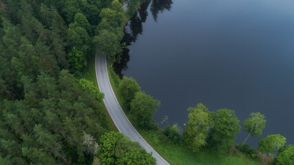 Top view of the curved road, green dark forest and the lake shore. Cloudy summer day. 