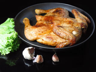 Fried roast chicken Tabaka in frying pan on black background. Garlic and salad.