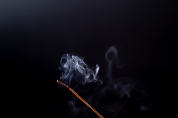 Incense stick with a wisp of smoke. On a dark background