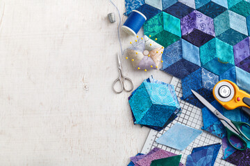 Fragment of tumbling blocks quilt, accessories for quilting on a white surface. Space for text.