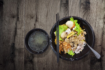 local dried pork noodles served with clear soup in black ceramic bowl on wooden background