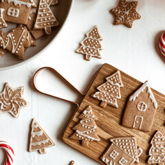 Homemade ginger cookies (stars, fir trees, houses) on wooden cutting board, stick candies, Christmas bauble. Flat lay, top view Christmas / New Year composition.