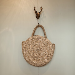 Straw bag hang on deer horns hanger on beige wall. Minimalist interior design concept.