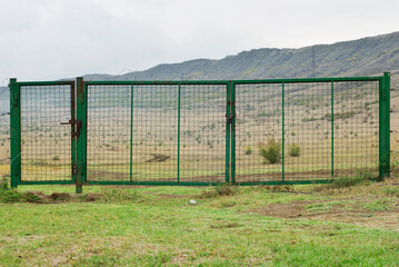 A green iron gate with a grid structure closed with a padlock. 