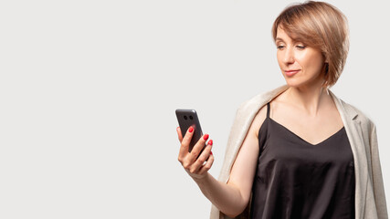 Fototapeta premium Mobile technology. Online communication. Female user. Social media. Confident business woman in smart casual outfit reading message on phone smiling isolated on light neutral copy space background.