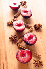 Sliced red plums with cinnamon sticks and anise stars on the wooden table. Selective focus. Shallow depth of field.