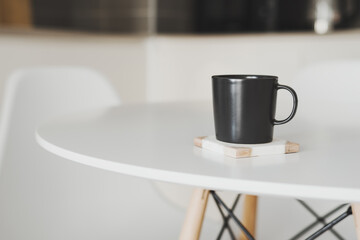 Empty black coffee mug stand on a marble coaster at the kitchen table