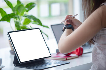 Fototapeta premium Cropped shot of Business women are using a tablet showing a white screen to put your text and pictures working on a table beside the window.
