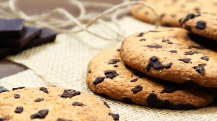 American chocolate chip cookies on a brown wooden table and on a linen napkin close-up. Traditional rounded crunchy dough with chocolate chips. Bakery. Delicious dessert, pastries. Rural still life.