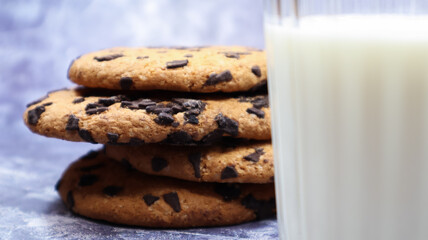 American chocolate chip cookies stacked on top of each other with milk in a glass on a gray background. Traditional rounded crunchy dough with chocolate chips. Bakery. Delicious dessert, pastries.