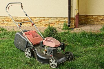 Fototapeta premium one lawn mower on the green grass near the wall of the building