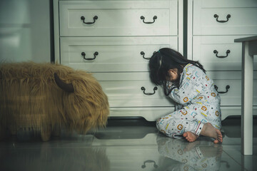 Sad little girl sitting on floor indoors. Child in danger. Sad little girl closing eyes with hands...