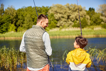 family, generation, summer holidays and people concept - happy smiling father and son with fishing rods on river
