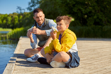 family, generation and food concept - happy smiling father and son with tablet pc computer eating sandwiches on river berth
