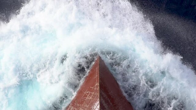 Aerail view of the bow of a merchant ship sailing at sea and creating splashes of sea water.