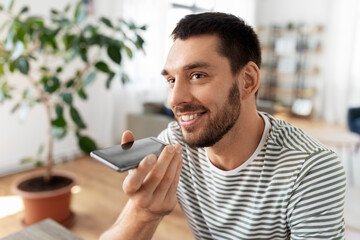 technology, remote job and people concept - happy smiling man calling on smartphone or using voice command recorder at home office
