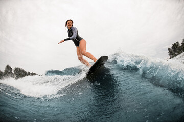 woman in black wetsuit stand on a surfboard and rides down on wave