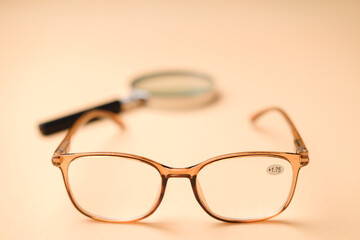 Orange eyeglasses for farsighted people with magnifying glass on an orange pastel background.