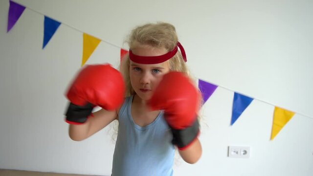Little girl kid kicks boxing gloves. Blond child looking at camera. Slow motion