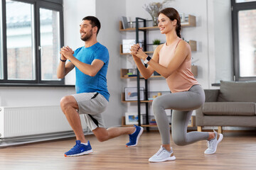 sport, fitness, lifestyle and people concept - smiling man and woman exercising and doing squats in low lunge at home
