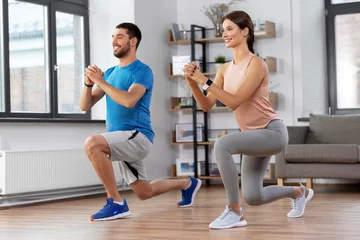 Foto op Canvas sport, fitness, lifestyle and people concept - smiling man and woman exercising and doing squats in low lunge at home © Syda Productions