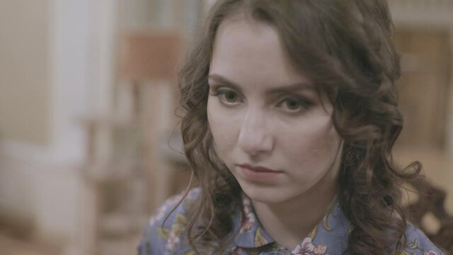 Close-up of young woman with frightened look. Stock. Young woman is nervous and looks away from table at home. Something is bothering young woman at family dinner