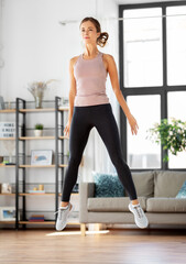 Fototapeta na wymiar sport, fitness and healthy lifestyle concept - young woman exercising and jumping at home