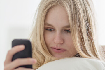 Pretty young woman texting online using her mobile phone in bed.
